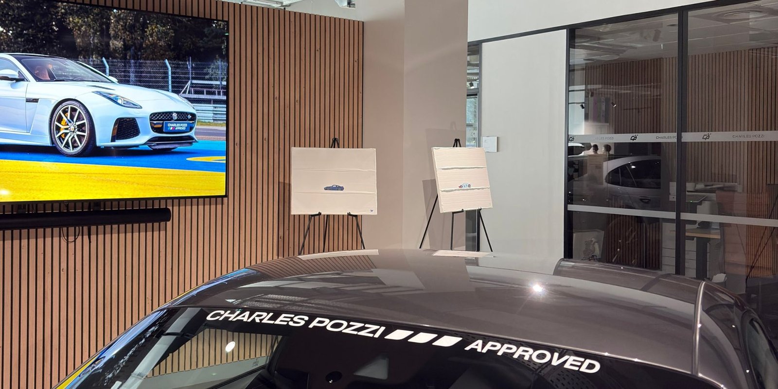 Deux tableaux de Jules Vincent exposés sur chevalet chez Charles Pozzi Approved, derrière une voiture de la concession.